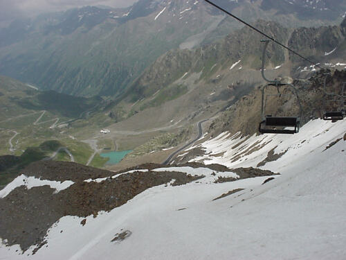 Blick vom Schneefeld auf einen grünen Alpensee.